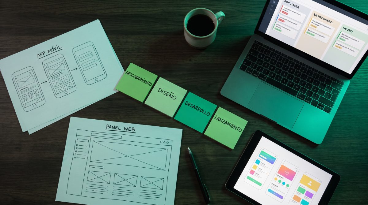 Sesión de planeación de un proyecto de software: bocetos de app y dashboard, notas adhesivas con etapas de descubrimiento, diseño, desarrollo y lanzamiento