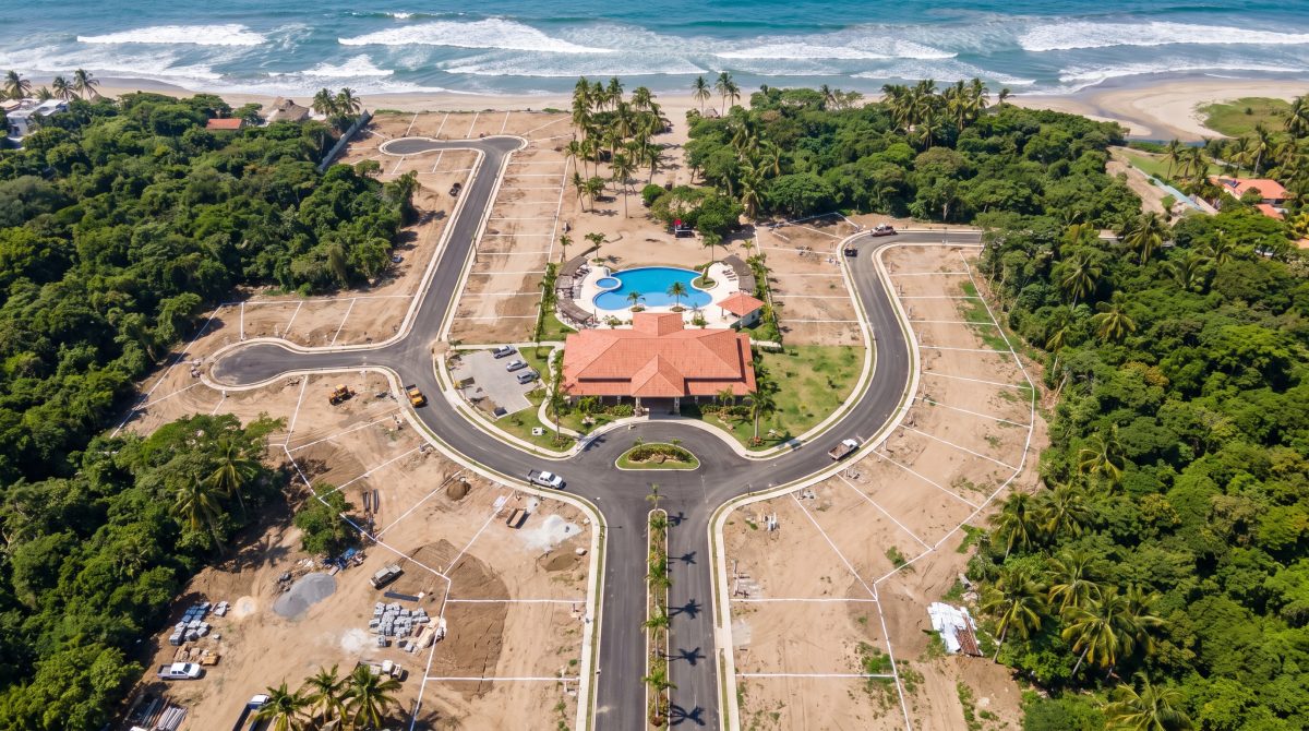 Vista cenital desde un dron de una lotificación residencial en construcción en la costa de Nayarit, con calles nuevas, casa club con alberca y selva alrededor.
